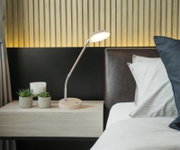 Moderne LED-Schreibtisch- bzw. Nachttischlampe in Beige mit flexiblem Schwanenhals auf einem Nachttisch neben dem Bett, Frontansicht leicht seitlich von links