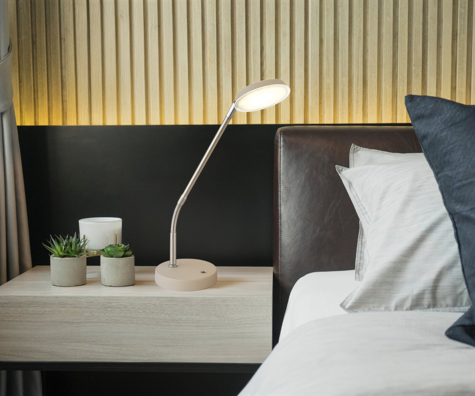 Moderne LED-Schreibtisch- bzw. Nachttischlampe in Beige mit flexiblem Schwanenhals auf einem Nachttisch neben dem Bett, Frontansicht leicht seitlich von links