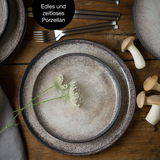 Vogelperspektive auf ein edles und zeitloses 18-teiliges Tafelservice in Beige mit rustikalem Design, dekoriert mit weißen Blüten und Pilzen auf einem Holztisch.