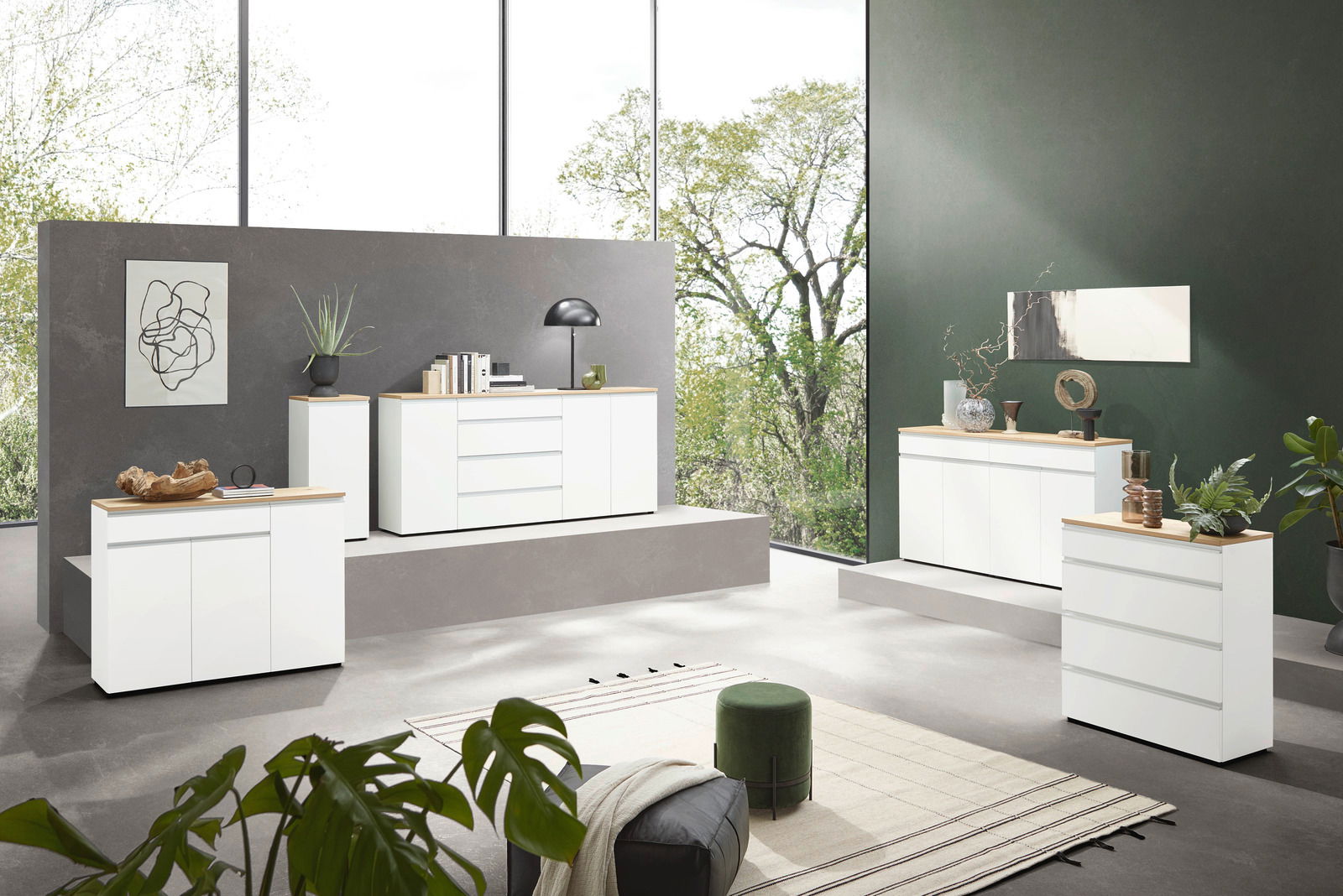 Moderne weiße Kommoden in einem stilvollen Wohnzimmer mit großen Fenstern und grüner Wand, seitliche Perspektive.