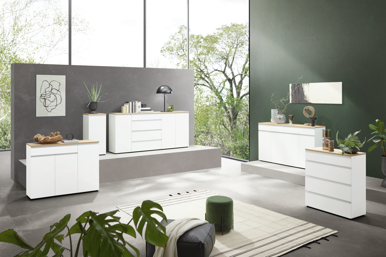 Moderne weiße Kommoden in einem stilvollen Wohnzimmer mit großen Fenstern und grüner Wand, seitliche Perspektive.