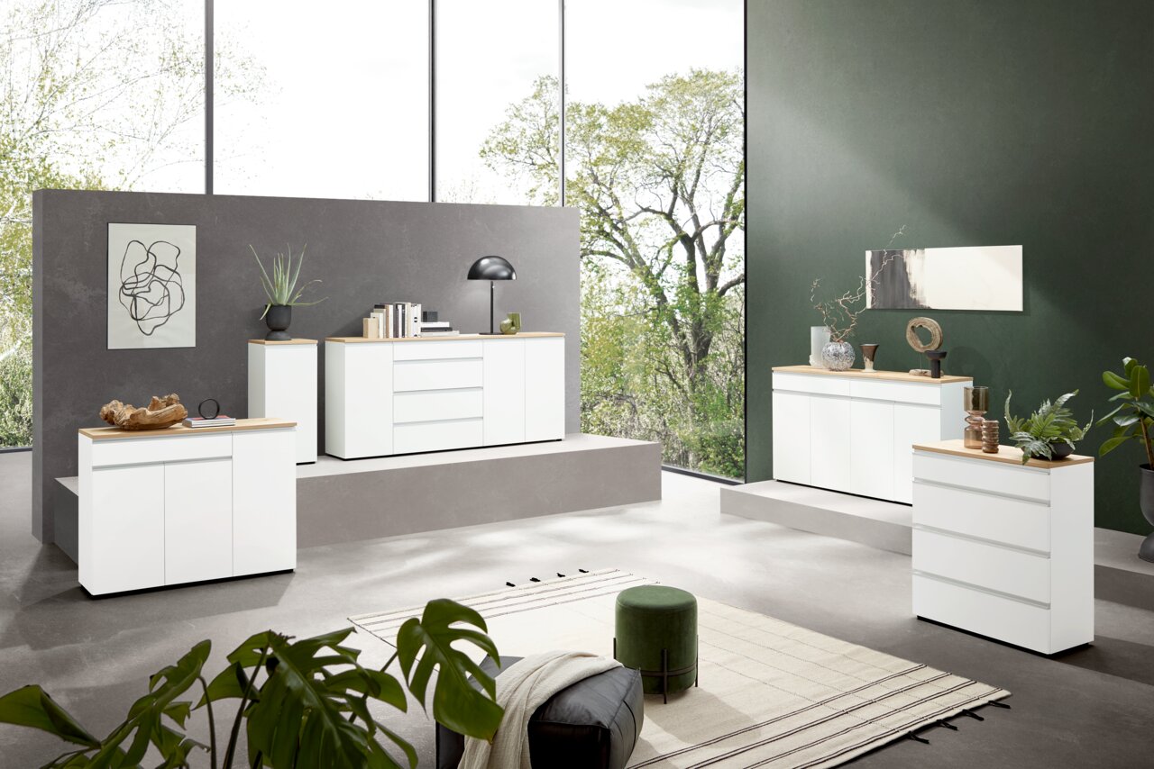Dieter Knoll Sideboard LENDINA Moderne weiße Kommoden in einem stilvollen Wohnzimmer mit großen Fenstern und grüner Wand, seitliche Perspektive.