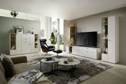 Moderne Wohnzimmeransicht mit eleganter weißer Vitrine, die von vorne sichtbar ist, neben einem großen Fernseher und stilvollen Möbeln.