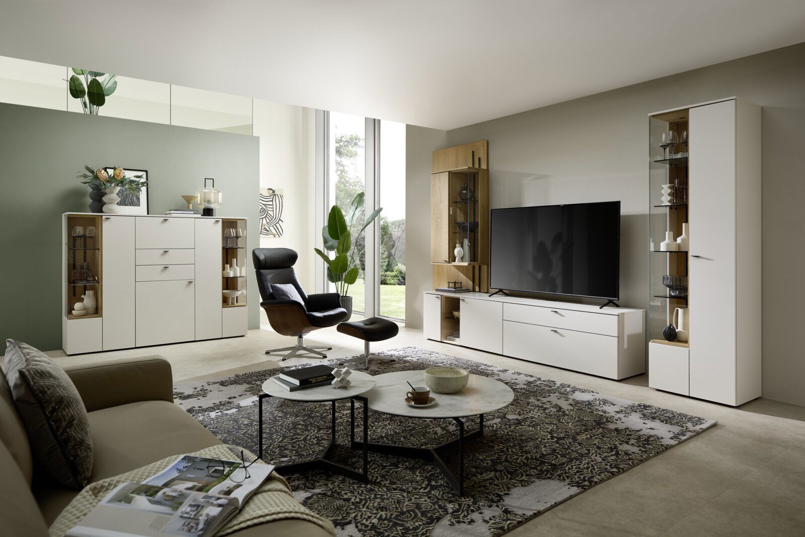 Moderne Wohnzimmeransicht mit eleganter weißer Vitrine, die von vorne sichtbar ist, neben einem großen Fernseher und stilvollen Möbeln.