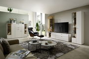 Moderne Wohnzimmeransicht mit eleganter weißer Vitrine, die von vorne sichtbar ist, neben einem großen Fernseher und stilvollen Möbeln.
