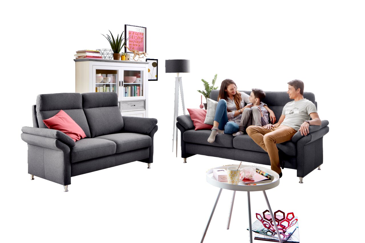 Wohnzimmer mit zwei grauen Sofas, eines davon mit einer Familie darauf, im Hintergrund ein weißes Regal und eine Stehlampe, Perspektive von vorne.