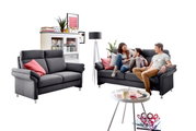 Wohnzimmer mit zwei grauen Sofas, eines davon mit einer Familie darauf, im Hintergrund ein weißes Regal und eine Stehlampe, Perspektive von vorne.