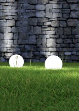 Zwei leuchtende Gartenkugeln auf einer Wiese vor einer Steinmauer, seitliche Perspektive.