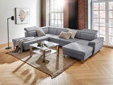 Graue Wohnlandschaft TIM in U-Form mit verstellbaren Kopfstützen, dekoriert mit Kissen und Decke, in einem modernen Wohnzimmer mit großen Fenstern und Holzboden, Perspektive von vorne links.