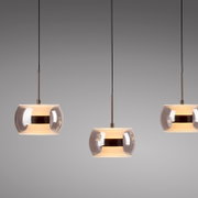 Drei moderne Pendelleuchten mit rauchgrauem Glas-Schirm und warmem Licht, frontal aus leicht unterer Perspektive vor grauem Hintergrund