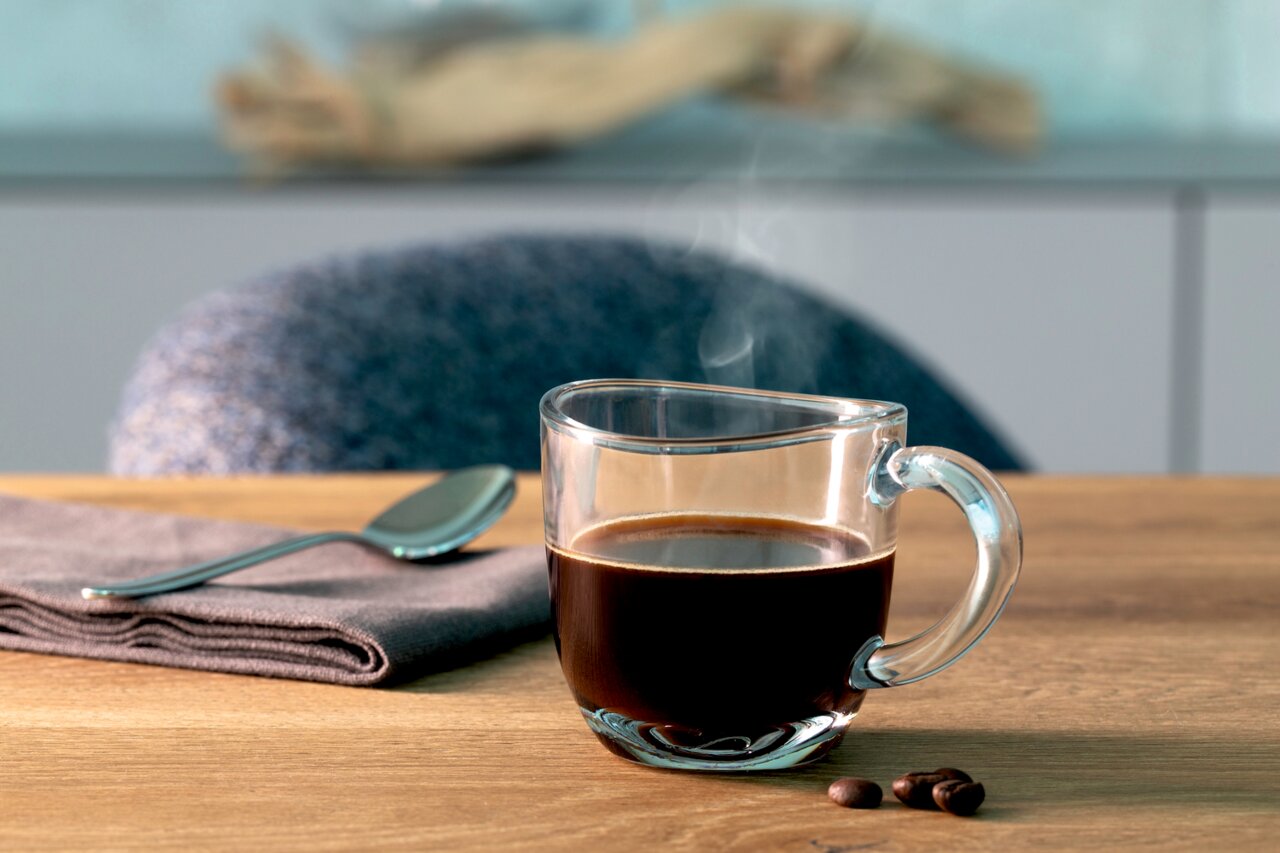 Leonardo Espressotasse NAPOLI Espressotasse Napoli 80ml aus Glas, gefüllt mit heißem Espresso, auf einem Holztisch mit Löffel und Serviette, seitliche Perspektive.