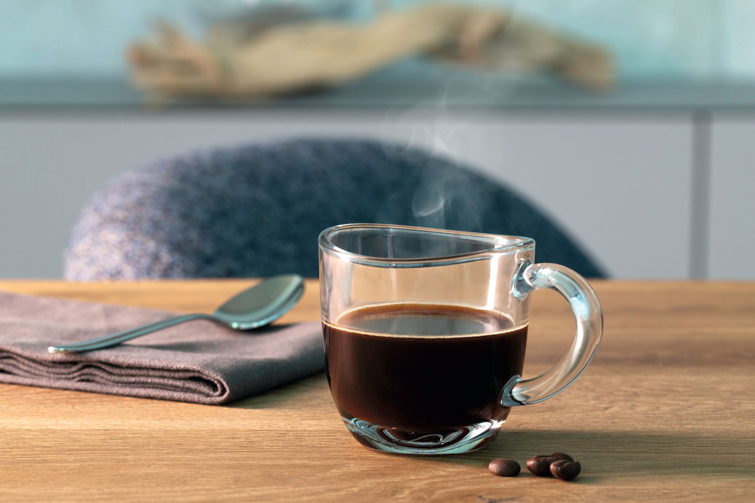 Espressotasse Napoli 80ml aus Glas, gefüllt mit heißem Espresso, auf einem Holztisch mit Löffel und Serviette, seitliche Perspektive.