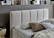 Seitliche Ansicht eines modernen Polsterbetts mit beigem Kopfteil und dekorativen Kissen.