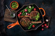 Grillpfanne in Ofenrot mit gegrilltem Fleisch, Radieschen und grünem Gemüse, von oben betrachtet.