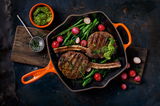 Grillpfanne in Ofenrot mit gegrilltem Fleisch, Radieschen und grünem Gemüse, von oben betrachtet.