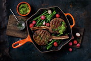 Grillpfanne in Ofenrot mit gegrilltem Fleisch, Radieschen und grünem Gemüse, von oben betrachtet.