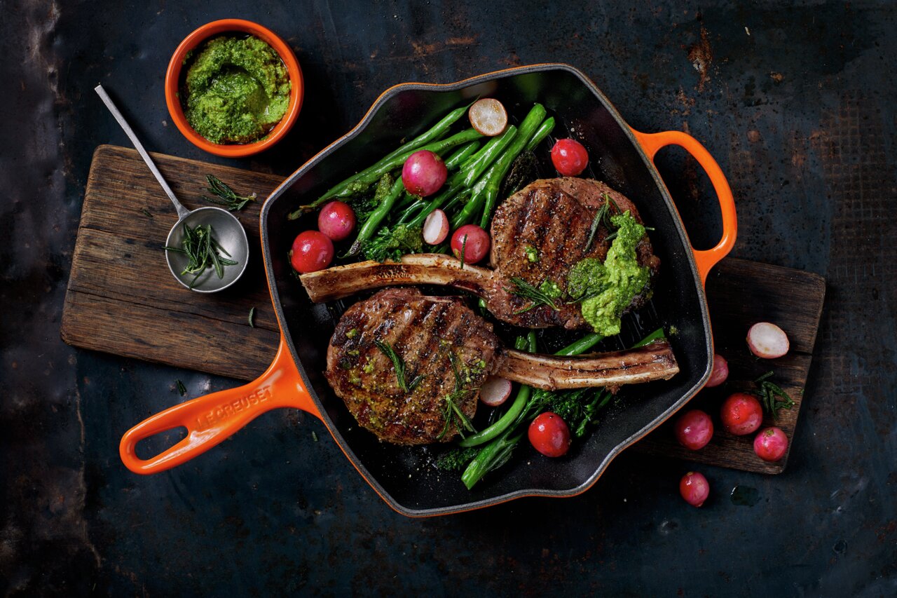 Grillpfanne in Ofenrot mit gegrilltem Fleisch, Radieschen und grünem Gemüse, von oben betrachtet.