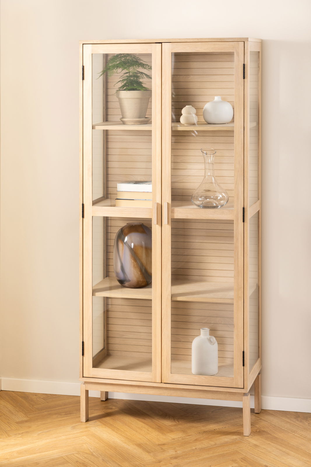 Holzvitrine mit Glastüren, frontal fotografiert, mit dekorativen Objekten auf den Regalen.
