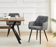 Gepolsterter Esszimmerstuhl in Grau mit Armlehnen und schwarzen Metallbeinen neben Holztisch, frontale Perspektive im hellen Wohnraum.