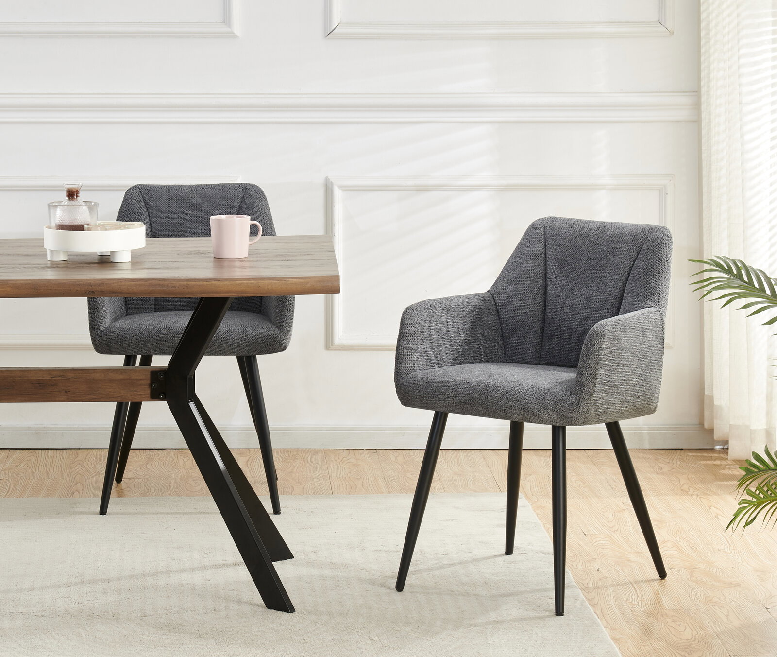 Gepolsterter Esszimmerstuhl in Grau mit Armlehnen und schwarzen Metallbeinen neben Holztisch, frontale Perspektive im hellen Wohnraum.