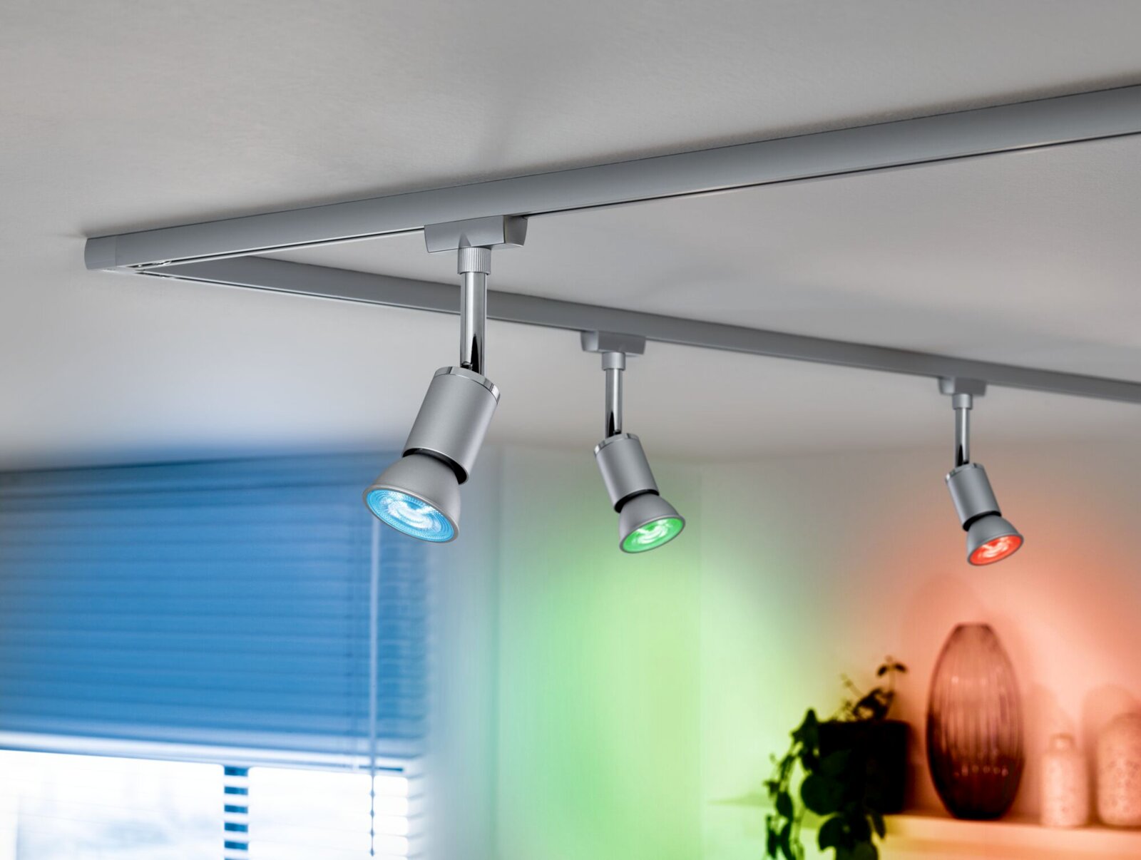 LED-Leuchtmittel in einer modernen Deckenleuchte mit drei Strahlern, die in verschiedenen Farben leuchten. Perspektive von unten.