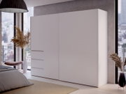 Moderner, weißer Schwebetürenschrank mit zwei Türen, seitliche Perspektive, in einem stilvoll eingerichteten Schlafzimmer mit großen Fenstern und Stadtblick.