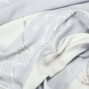 Detailfoto van een gordijn met oogjes en een elegant patroon in lichte tinten.
