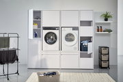 Moderner Doppel-Waschmaschinenschrank mit Waschmaschine und Trockner, umgeben von Regalen und Stauraum, aus frontaler Perspektive.