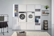 Moderner Doppel-Waschmaschinenschrank mit Waschmaschine und Trockner, umgeben von Regalen und Stauraum, aus frontaler Perspektive.