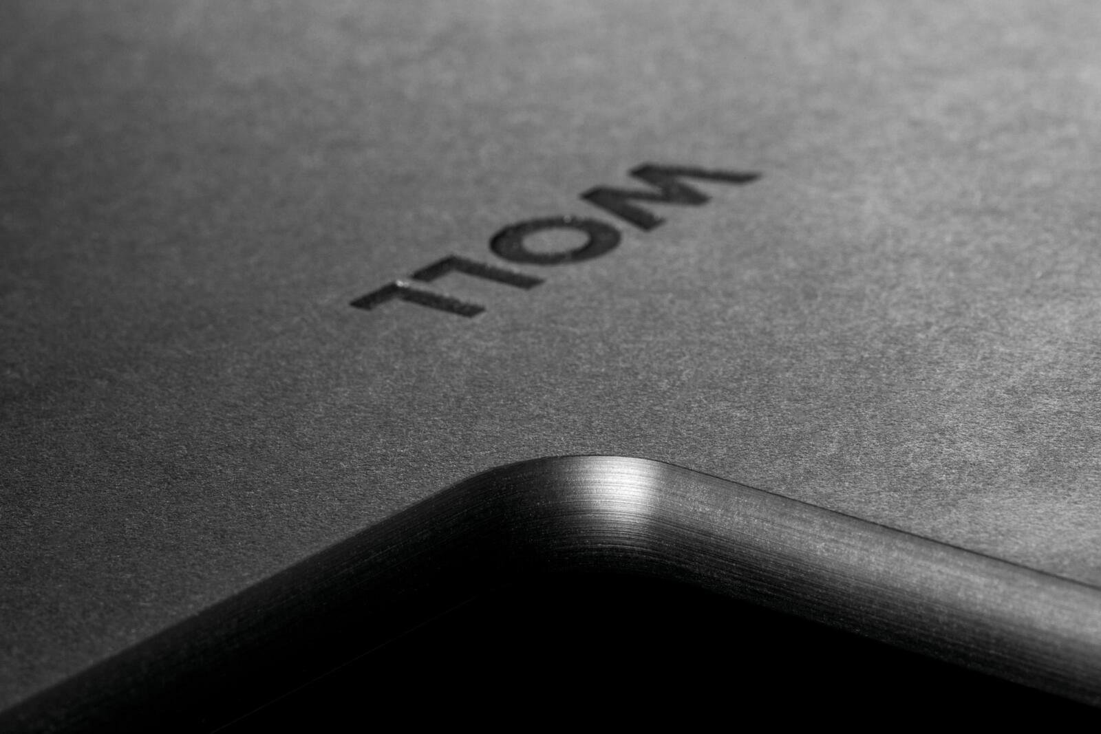 Nahaufnahme eines schwarzen Schneidebretts mit abgerundeter Ecke und eingeprägtem Schriftzug, perspektivisch von der Seite aufgenommen.