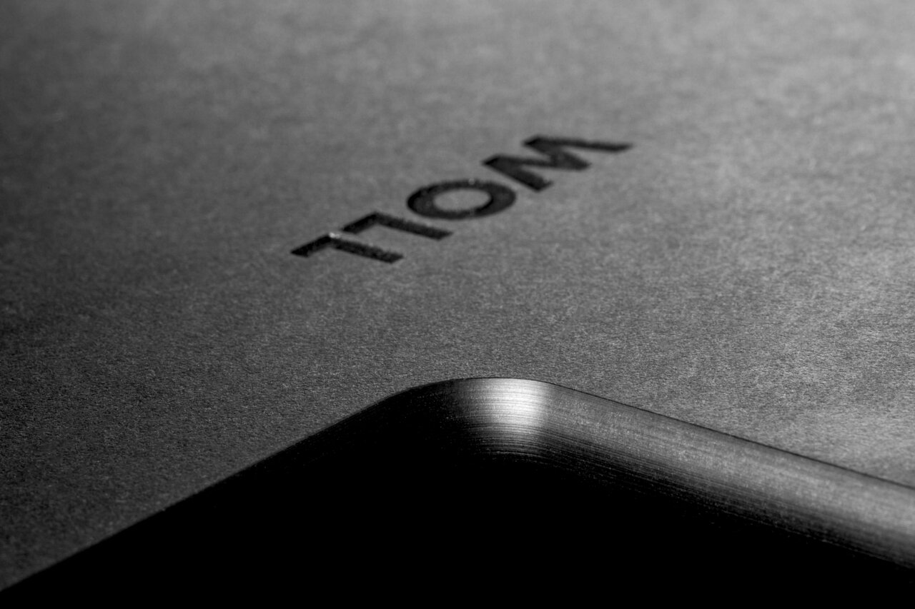 Nahaufnahme eines schwarzen Schneidebretts mit abgerundeter Ecke und eingeprägtem Schriftzug, perspektivisch von der Seite aufgenommen.