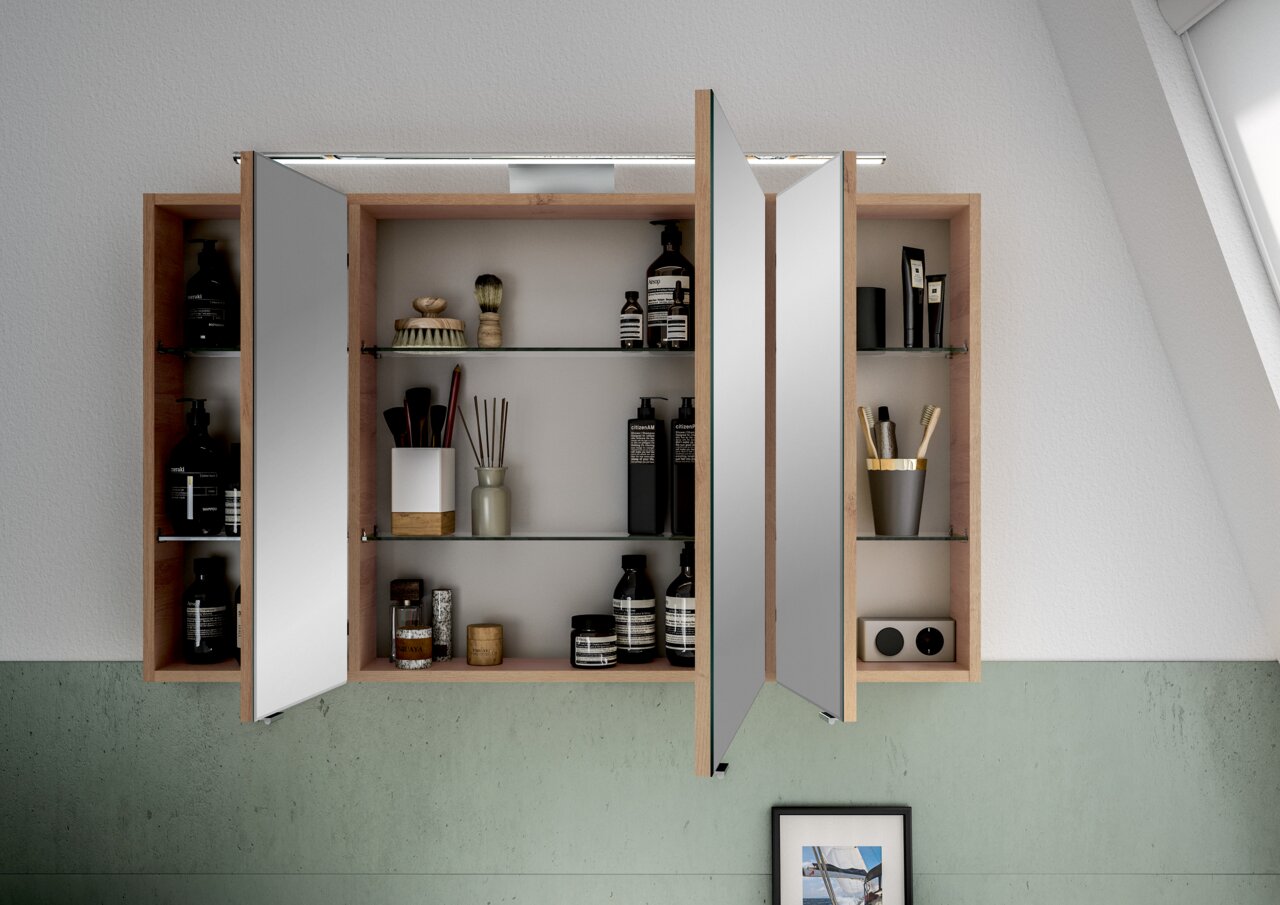 Offener Spiegelschrank mit Holzrahmen, gefüllt mit Pflegeprodukten und Accessoires, aus frontaler Perspektive.