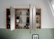 Offener Spiegelschrank mit Holzrahmen, gefüllt mit Pflegeprodukten und Accessoires, aus frontaler Perspektive.