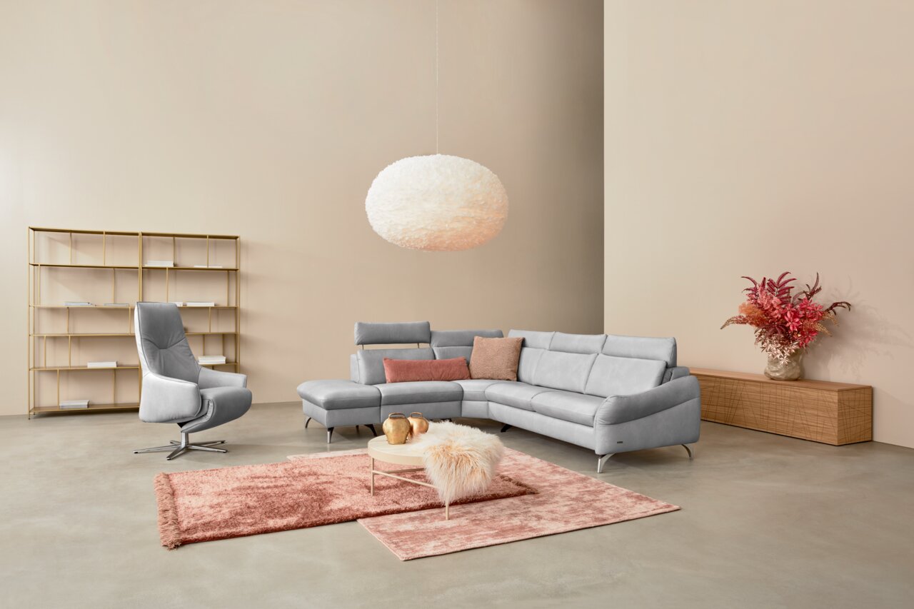 Himolla Ecksofa 1177 SPEKTRA Moderne Polsterrundecke in hellgrauem Stoff, aus der Perspektive von vorne rechts, mit dekorativen Kissen und einem eleganten Sessel daneben.