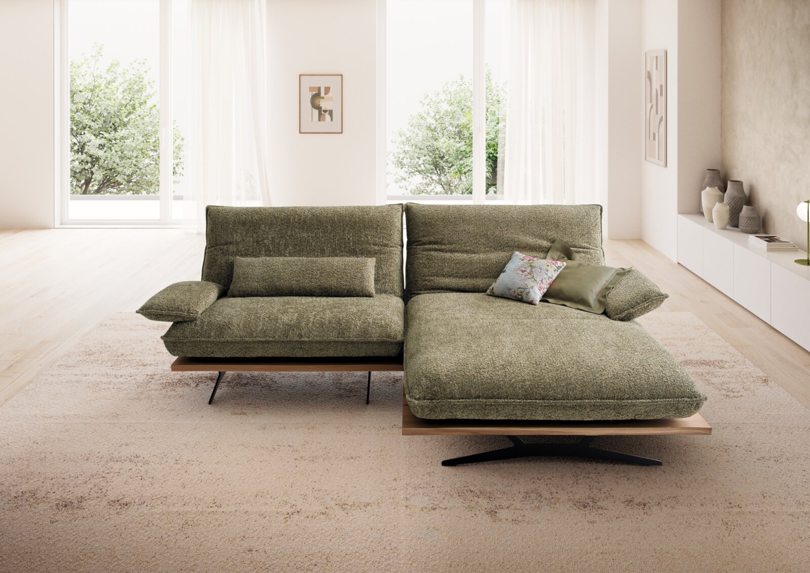 Modernes grünes Stoff-Ecksofa mit rechter Ottomane, niedriger Rückenlehne und Holzsockel auf hellem Teppich im lichtdurchfluteten Wohnzimmer, Frontansicht auf Sitzfläche und Polster