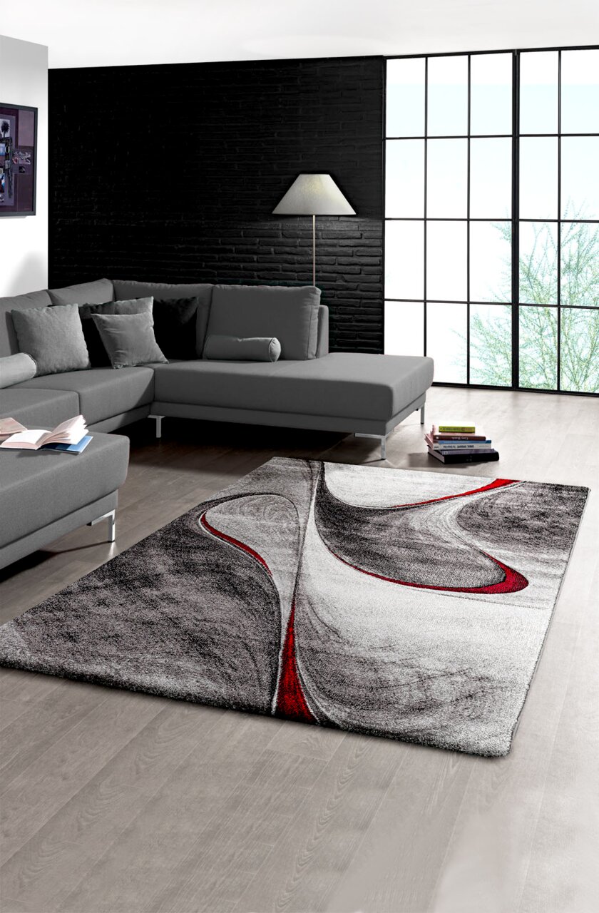 Moderner Teppich mit abstraktem Design in Schwarz, Weiß und Rot in einem stilvollen Wohnzimmer, Perspektive von oben.