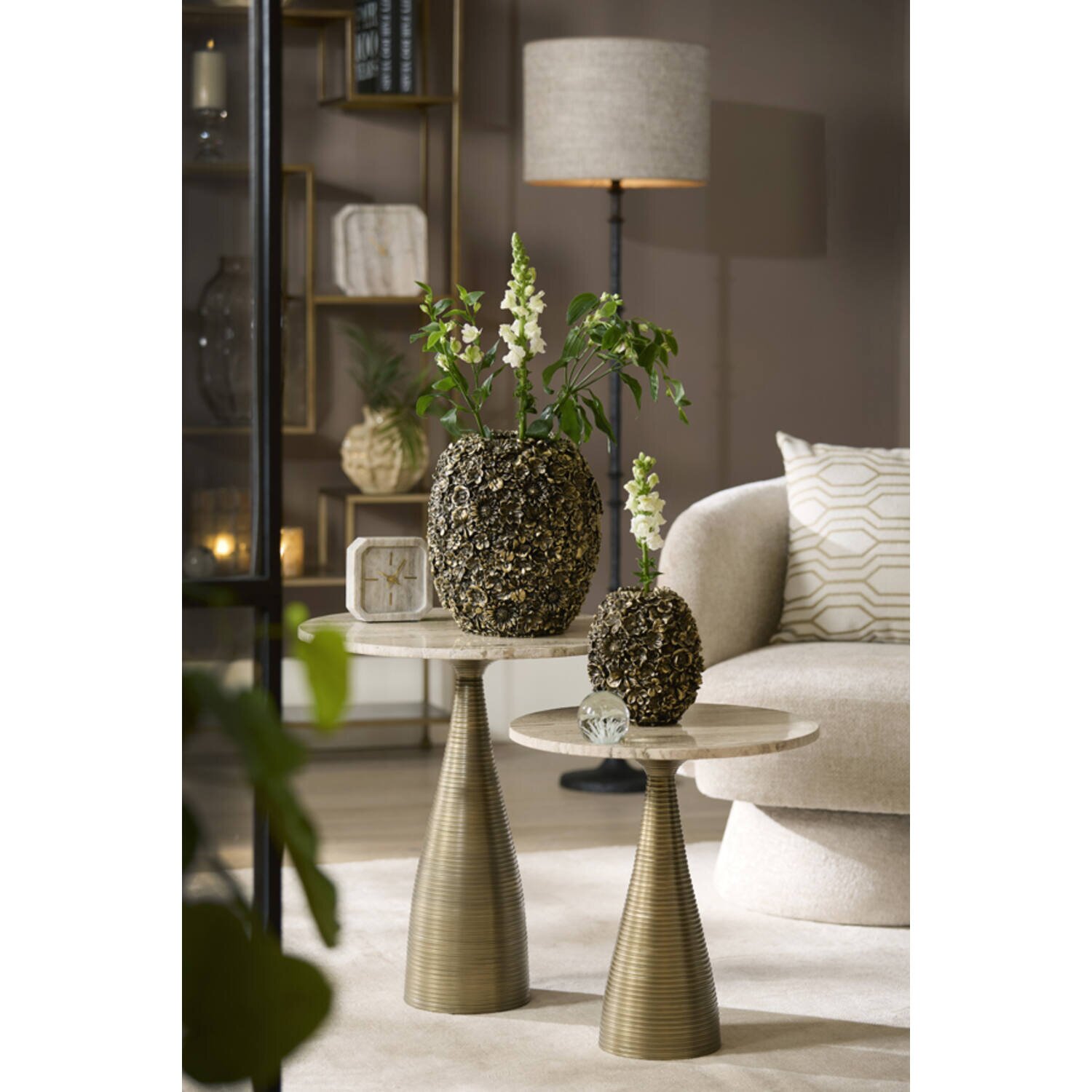 Twee ronde bijzettafels met een marmerachtig blad en een conische, goudkleurige geribbelde voet, versierd met gestructureerde vazen en witte bloemen in de woonkamer; perspectief: vooraanzicht op ooghoogte.