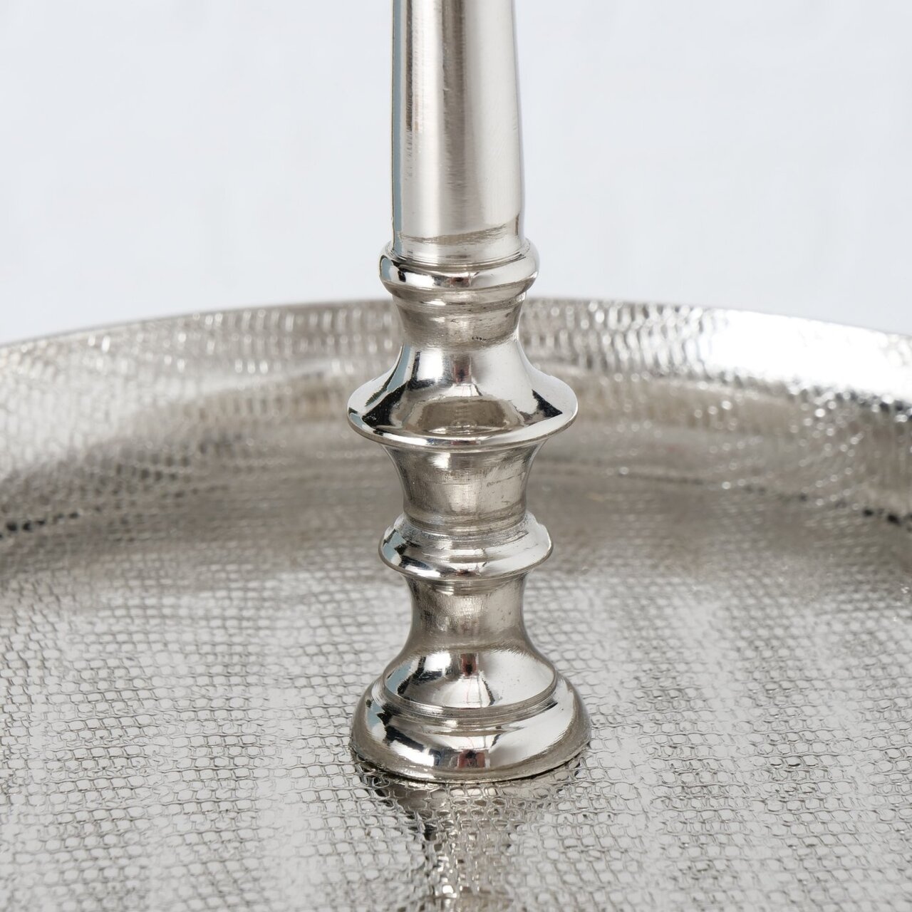 Nahaufnahme einer silbernen Etagere aus Aluminium mit strukturierter Oberfläche und elegantem Mittelstab, seitliche Perspektive.