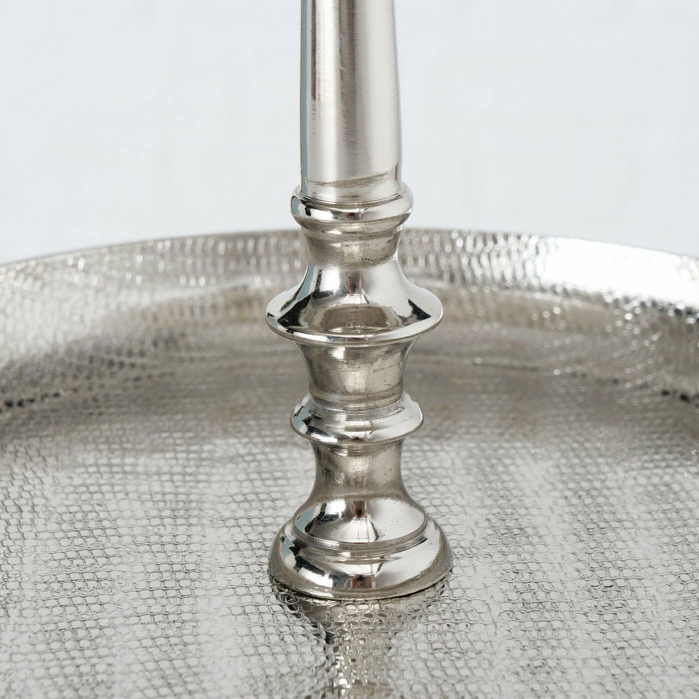 Nahaufnahme einer silbernen Etagere aus Aluminium mit strukturierter Oberfläche und elegantem Mittelstab, seitliche Perspektive.