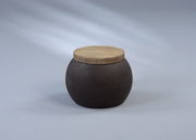 Runder Beistelltisch mit dunklem, strukturiertem Korpus und heller Holzplatte, seitliche Perspektive