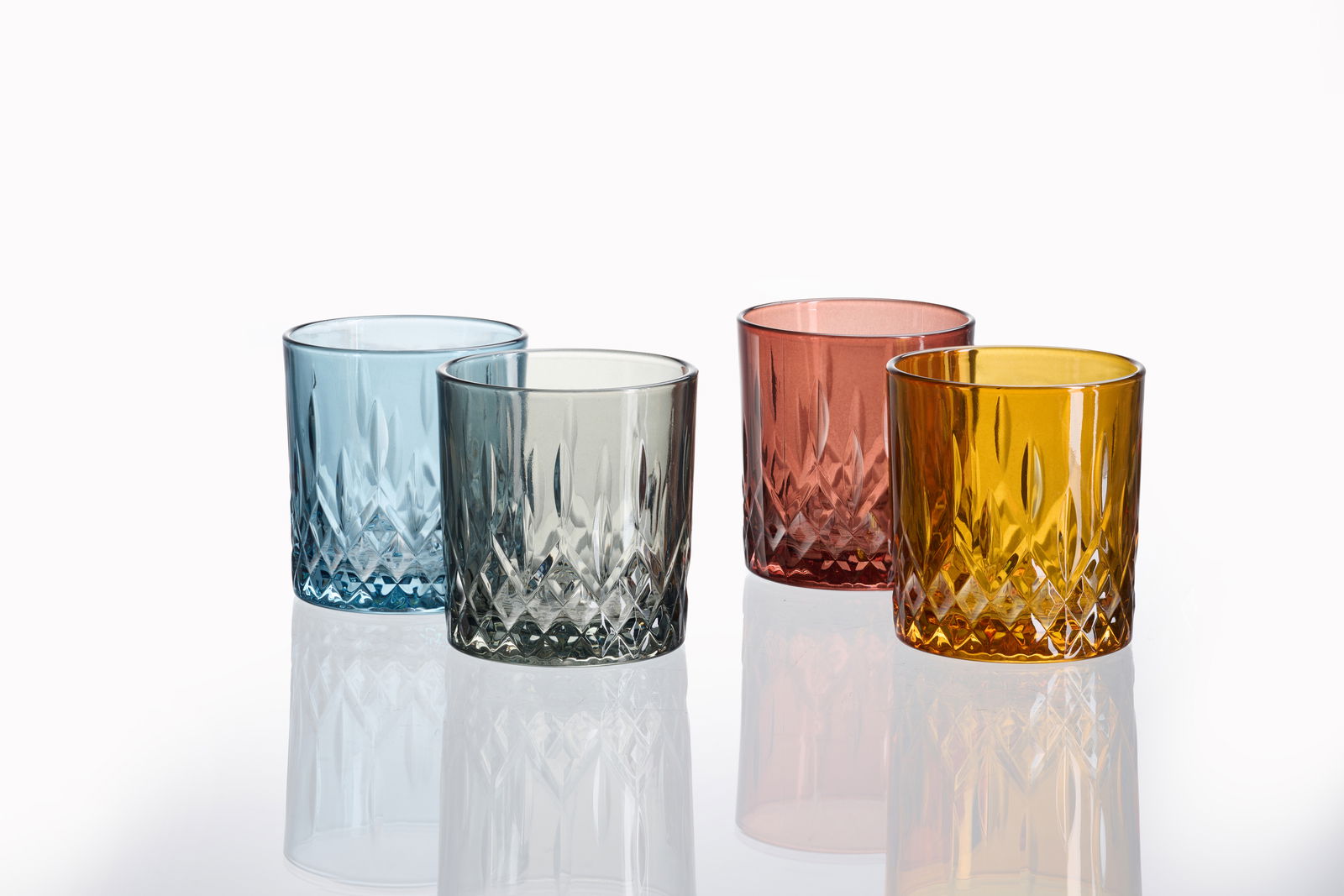 Vier Whiskygläser in verschiedenen Farben (blau, grau, rot, gelb) mit facettiertem Design, aus einer leicht erhöhten Perspektive fotografiert.