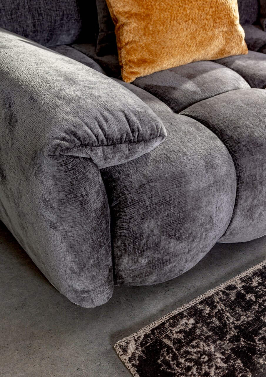 Nahaufnahme eines grauen Megasofas mit weicher Polsterung und einem orangefarbenen Kissen, seitliche Perspektive.