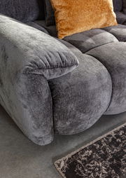 Nahaufnahme eines grauen Megasofas mit weicher Polsterung und einem orangefarbenen Kissen, seitliche Perspektive.