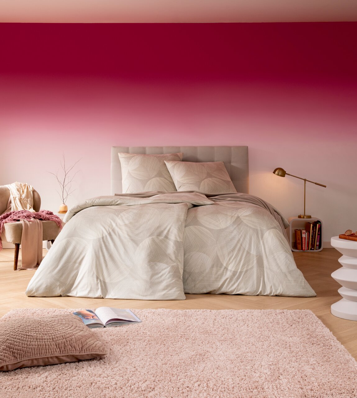 Estella Bettwäsche DORA Gemütliches Schlafzimmer mit einem Doppelbett in sanften Beige- und Cremetönen, dekoriert mit einem modernen Muster. Im Vordergrund ein flauschiger Teppich und ein Kissen. Die Perspektive zeigt das Bett frontal mit einem harmonischen Farbverlauf an der Wa