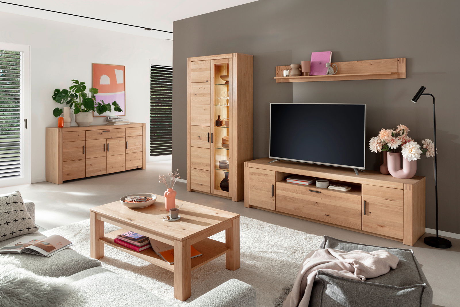 Moderne Wohnzimmeransicht mit einer Kombi-Vitrine aus Holz, die von vorne gezeigt wird. Die Vitrine ist Teil einer stilvollen Einrichtung mit einem Fernseher, einem Couchtisch und Dekorationen.