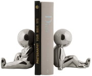 Twee zilveren boekensteunen in de vorm van zittende figuren die boeken rechtop houden. Aanzicht vanaf de zijkant.