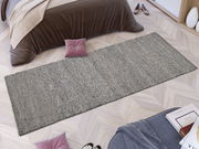 Handgewebter Teppich in Grau, rechteckig, auf hellem Holzboden vor einem Bett mit brauner Decke, aus der Vogelperspektive.