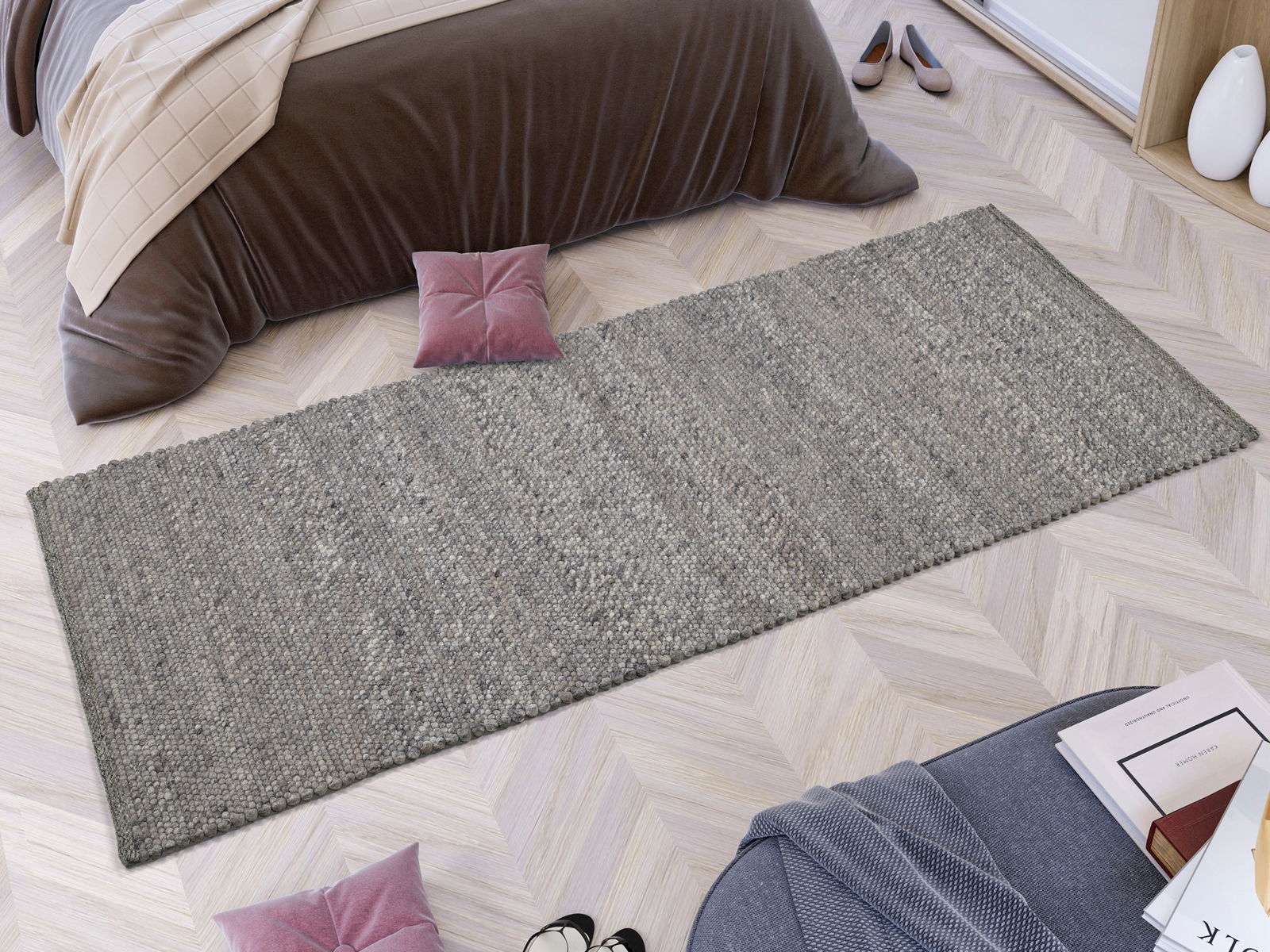 Handgewebter Teppich in Grau, rechteckig, auf hellem Holzboden vor einem Bett mit brauner Decke, aus der Vogelperspektive.