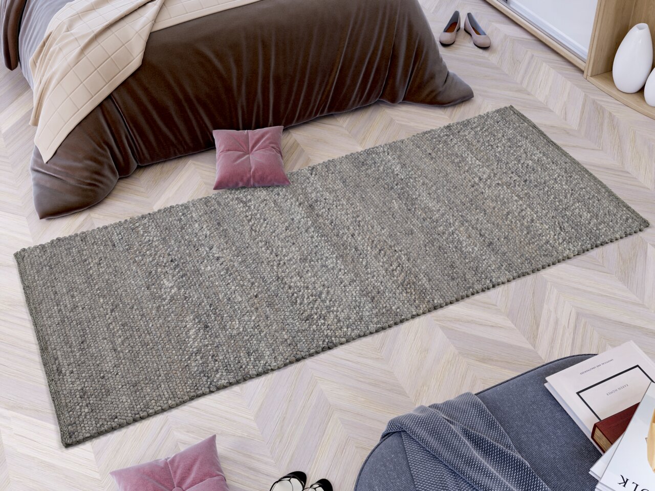 Handgewebter Teppich in Grau, rechteckig, auf hellem Holzboden vor einem Bett mit brauner Decke, aus der Vogelperspektive.