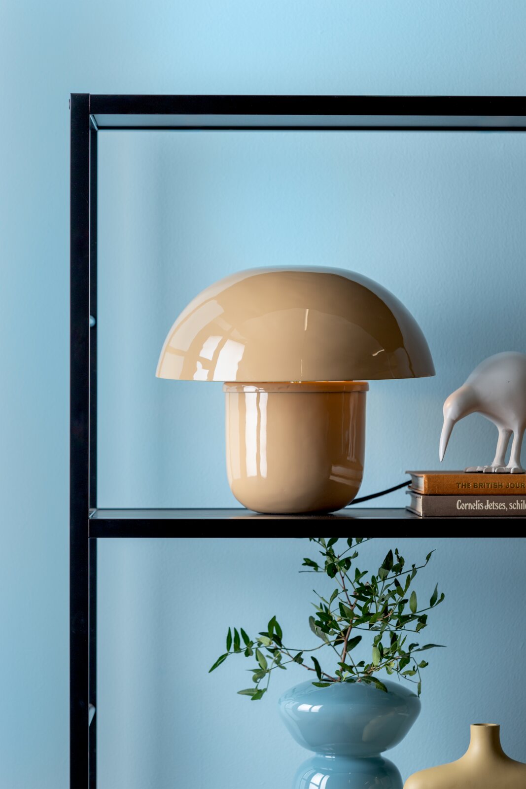Beige Tischleuchte mit Pilzform auf einem Regal, seitliche Perspektive